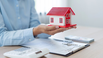 The real estate concept the realtor presenting his work towards his customer by putting the red house model on his palms and raising his hands a little