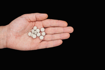 Male hand holding pills. Capsules are white. Medicines. Isolate on a black background. A remedy for diseases. Drug addiction concept. Treatment of illness with medication.