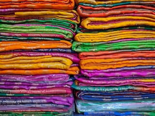 Closeup view of stacked colours saris or sarees in display of Indian retail shop, textile shop.