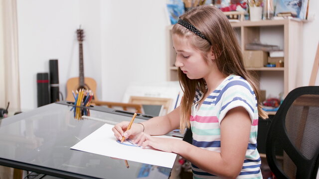 Young artist holding graphic pencil drawing colorful picture for art school homework sitting at desk. Cheerful child painter painting abstract sketch enjoying artistic lesson. Educational hobby