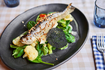 Roasted pike perch or cod fish with baked vegetables and spinach. Dish decorated with a slice of lemon. Restaurant menu