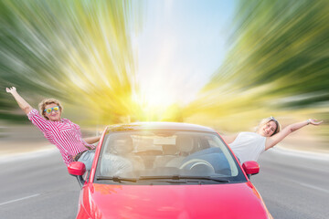 Two wild and crazy Caucasian women with their rental car on the freeway sitting in the doors sticking their bodies out of the vehicle. Thelma and Louise type wild vacation concept