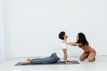 woman teaches man doing gymnastics yoga asana in a white room