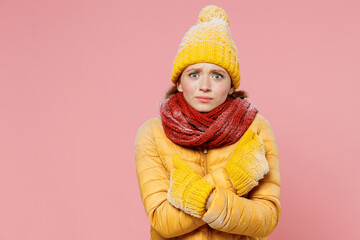 Frightened afraid scared astonished young woman 20s years old wear yellow jacket hat mittens looking camera holds hands crossed frowning isolated on plain pastel light pink background studio portrait