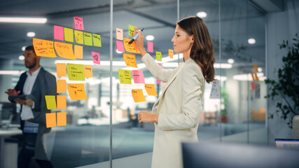 Young Confident Businesswoman Creating Project Plan on Office Wall with Paper Notes. Stylish...