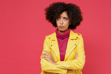 Obraz na płótnie Canvas Frowning angry sad young curly black latin woman 20s years old wear yellow jacket looking camera hold hands crossed isolated on plain red background studio portrait. People emotions lifestyle concept