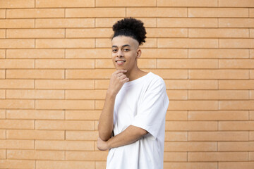 Gesture, lifestyle, expression and people concept. A handsome young African-American man, holding hand to his face, wearing a white T shirt on a brick wall background