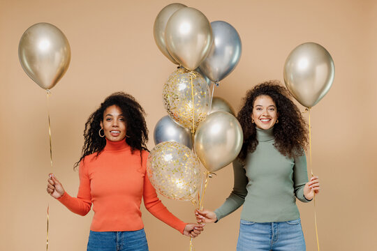 Two fun young curly black women friends 20s wear casual shirts clothes celebrating holiday party hold bunch of colorful air helium balloons isolated on plain pastel beige background studio portrait
