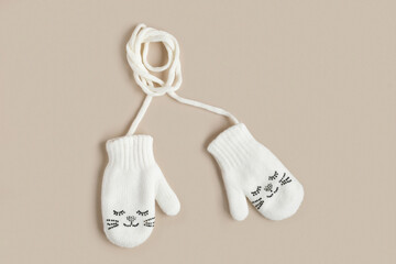 White knitted baby mittens isolated on a natural beige background, top view. Winter kids clothes....