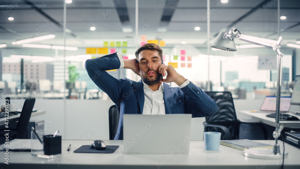 Poster young happy businessman using computer and talking on a phone in modern office. successful handsome 