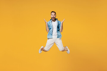 Fototapeta na wymiar Full body young surprised overjoyed excited happy caucasian man 20s wear blue shirt white t-shirt jump high spread hands isolated on plain yellow background studio portrait. People lifestyle concept.