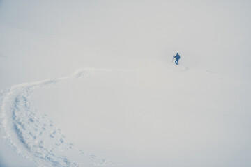 Male hiker in the distance in a vast minimalist winter scene with a footpath made in the snow leading towards him