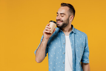 Young smiling happy man 20s wearing blue shirt white t-shirt hold takeaway delivery craft paper brown cup coffee to go isolated on plain yellow background studio portrait. People lifestyle concept
