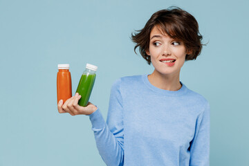 Young uncertain woman wear casual sweater hold pressed juice green orange vegetable smoothie as...