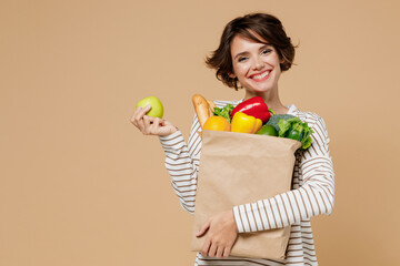 Young smiling vegetarian cheerful woman 20s in casual clothes hold paper bag with vegetables...