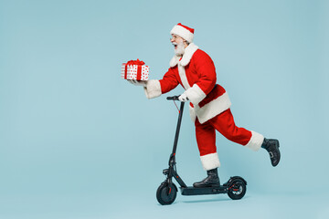 Full body fun old Santa Claus man 50s in Christmas hat red suit clothes rides kick scooter with...