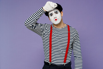 Sick ill young mime man with white face mask wears striped shirt beret put hands on head having headache suffer from migraine feel bad isolated on plain pastel light violet background studio portrait.