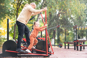 A man with his child, his little daughter, performs exercises on the sports ground of the city, the concept of an active healthy lifestyle in the family. teaching children exercises and training - obrazy, fototapety, plakaty