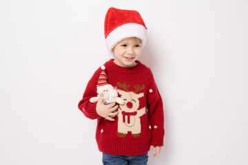 Little boy wearing santa hat holding santa claus toy standing over white background.