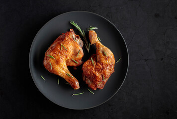 Grilled chicken legs sprinkled with rosemary on a black plate.