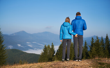 Back view of family pair in same clothing standing on stone trail of hill's top and admiring...