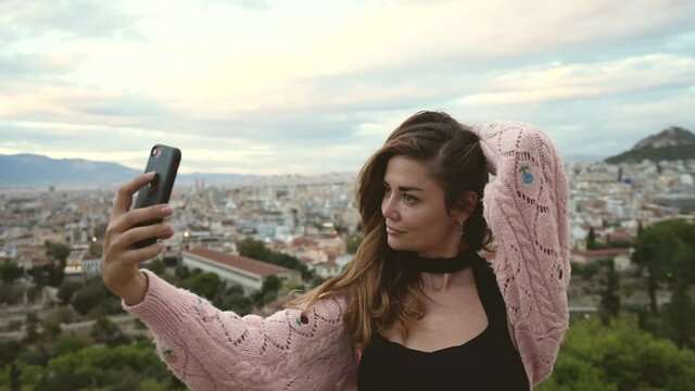 Young adult female traveling tourist with phone takes selfie with Acropolis hill, ruins of Athens. Traveler in vacation trip photographs Greece, shoots iphone pictures of herself. Temples tourism.