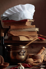 Fototapeta na wymiar Chef's hat, vintage cookbooks, and old kitchen utensils on the kitchen table.