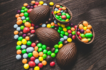 Chocolate easter eggs and colored sweets on a wooden background.