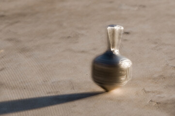 Obraz na płótnie Canvas A small, silver Hanukkah dreidel in motion as it spins on a stone surface.