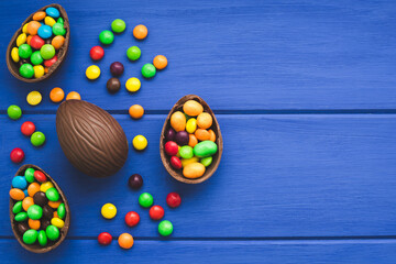 Chocolate easter eggs and colored sweets on a blue wooden backgorund. Place for text or logo.