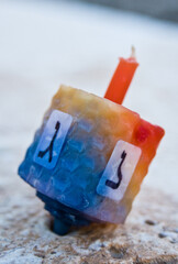 Orange and blue Hanukkah dreidel candle made from beeswax and resting on a stone surface. 