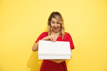 Young, beautiful long-haired blonde woman in red dress, joyfully opens white box with space for an inscription. Surprise concept. Love shopping, shopaholic.