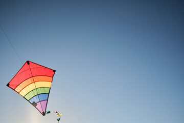 Windy weather is great time to play with kite. Empty minimalistic background. Multicolored striped kite flies in blue sky.