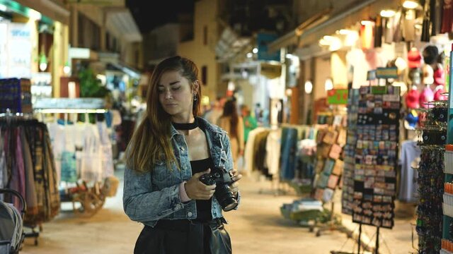Young adult female tourist photographer taking photos with camera during traveling vacation to Greece. Tourism time. Traveler woman on evening streets of Greek Athens. Cozy dusk holidays atmosphere.