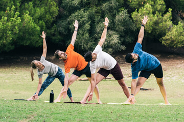 People doing the triangle pose of yoga in a park