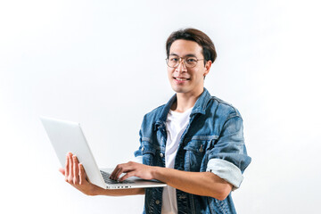Succeed Asian young man on a blue jeans jacket standing and using a laptop, cheerful. A man with excellent financial results is happy working in a modern office on a computer over white background