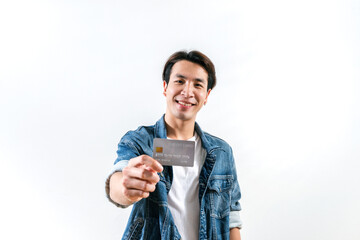 A young man smiles and looks happy with a credit card in hand, he is looking away while showing and...