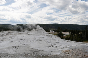Yellowstone National Park.
Bubbling blue water inside the deep cone of a geyser, with some smoke.