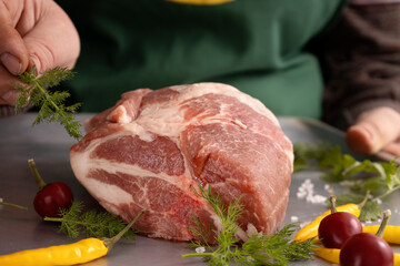 Closeup of piece of pork meat,green fresh dill,silantro,pepper on the oven tray.Woman preparing meat for baking