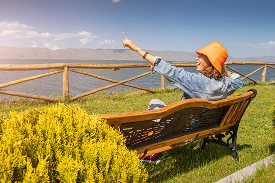 Young woman sitting on the bench and pointing to the Sevan Lake