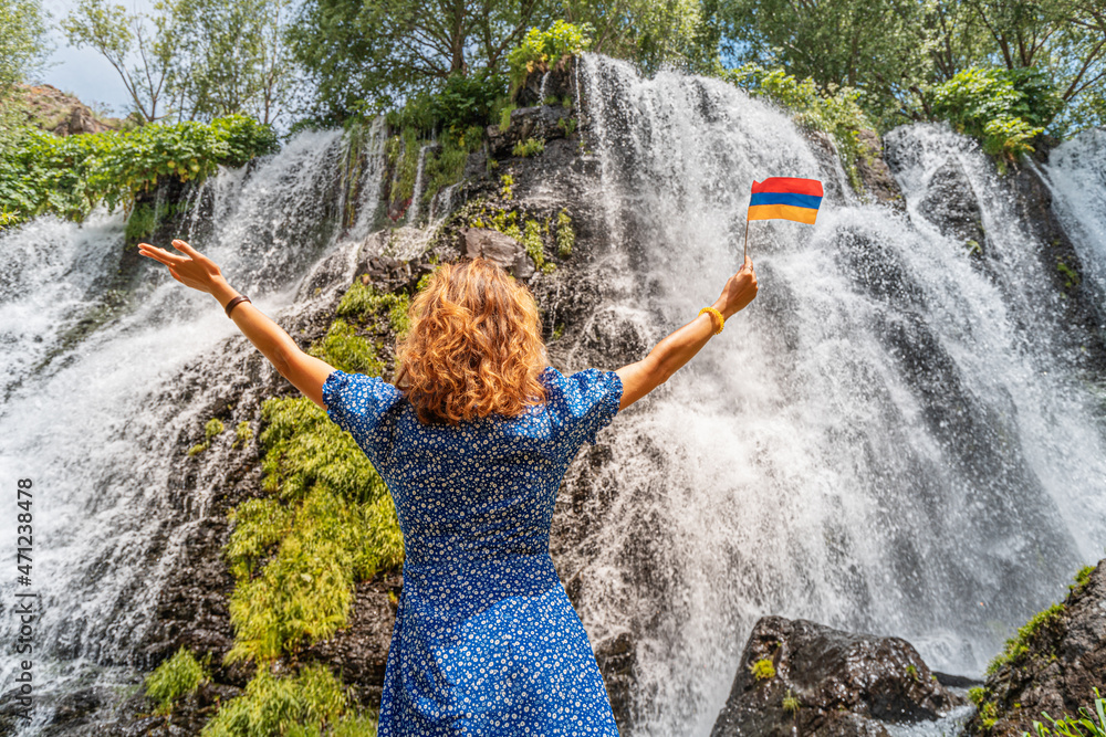 Wall mural happy woman traveler with armenian flag is resting near the beautiful and large shaki waterfall in a