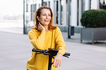 Happy middle-aged woman using an electric scooter in town