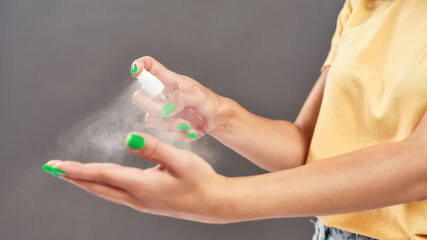 Closeup of female hands. Woman applying sanitizer alcohol spray on hands isolated over gray background