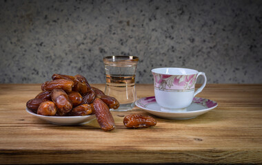 A coffee cup with a saucer, a glass of water and date fruits on a saucer on a wooden table
