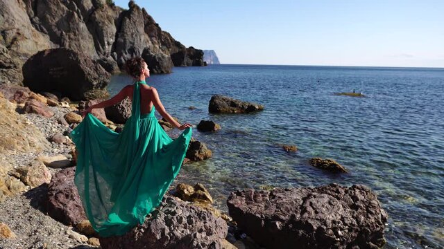 Side view a Young beautiful sensual woman with black hair in a long mint dress posing on a beach with calm sea bokeh lights on sunny day. Girl on the nature on blue sky background. Fashion photo