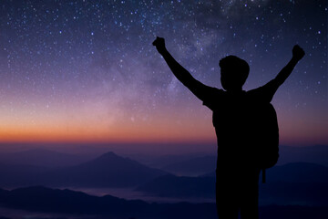 Silhouette of young traveler standing and open both arm watched night sky view, star and milky way alone on top of the mountain. He enjoyed traveling and was successful when he reached the summit.
