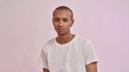 Portrait of young mixed race man in casual white t shirt looking at camera, standing isolated over...