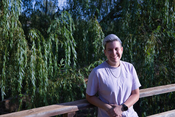 Portrait of a non-binary person, smiling and leaning on a wooden railing outdoors. Non binary concept, lgbtq+, inclusion, gay, lesbian, lgbtq.