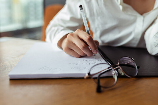 Unrecognizable crop businesswoman writing in notebook and making plan while working at table in cafe 