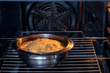 A dish in a metal bowl in the oven with a lush cheese brown crust. Abstract concept of baking a dish of fish, vegetables in sauce. Background